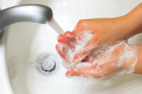 Waschbecken mit laufendem Wasserhahn und eingeseiften Händen beim Hände waschen